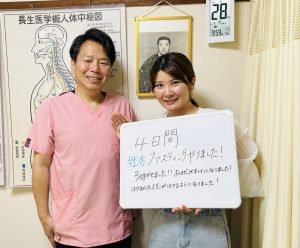 4日間の妊活ファスティング終了後、感想を書いたホワイトボードを持つ患者さんと江口長生治療院の院長